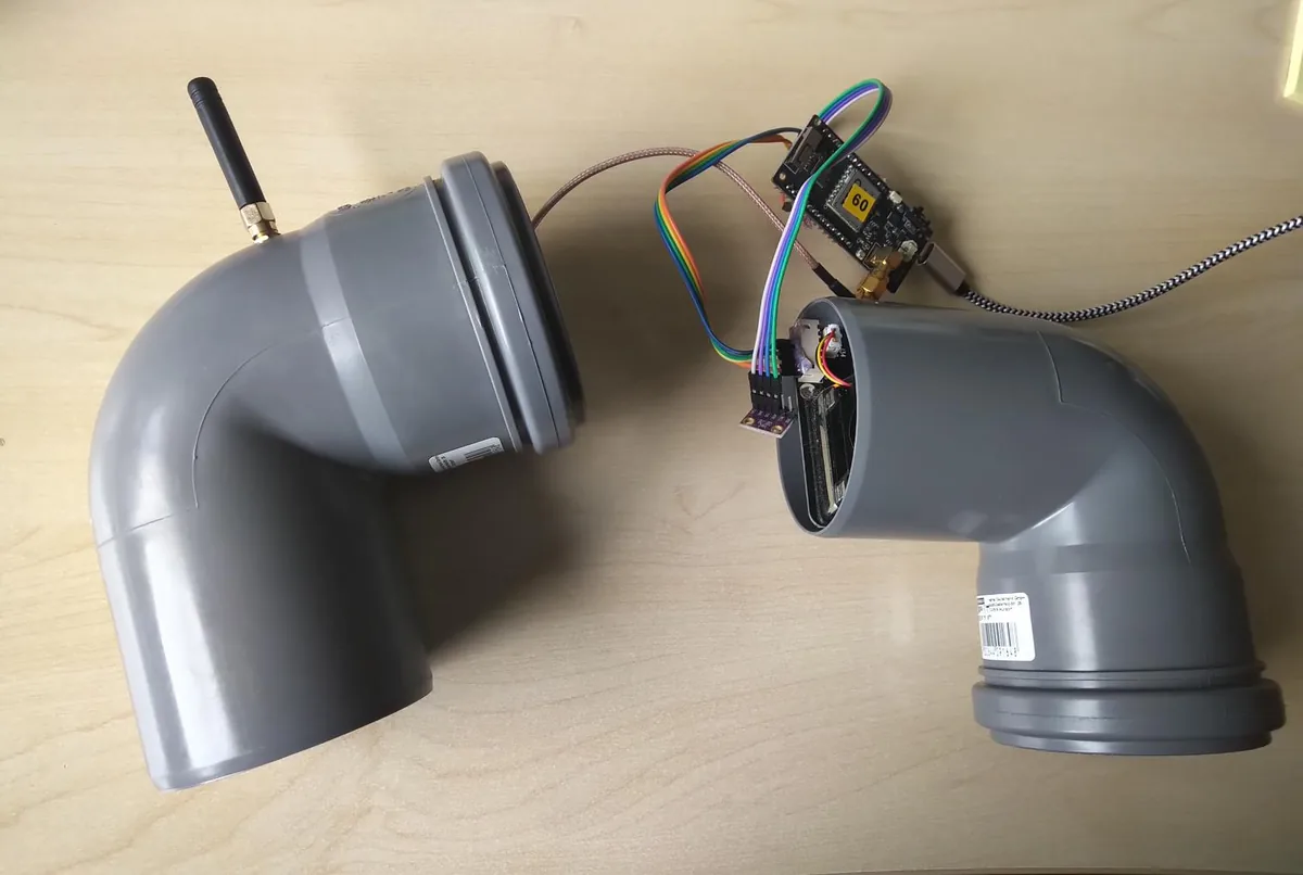 Geöffnete Sensorstation: zwei graue Rohrbögen als Gehäuse, darin Sensorik, verbunden über Kabel mit einem Mikrocontroller mit Funkmodul und Antenne